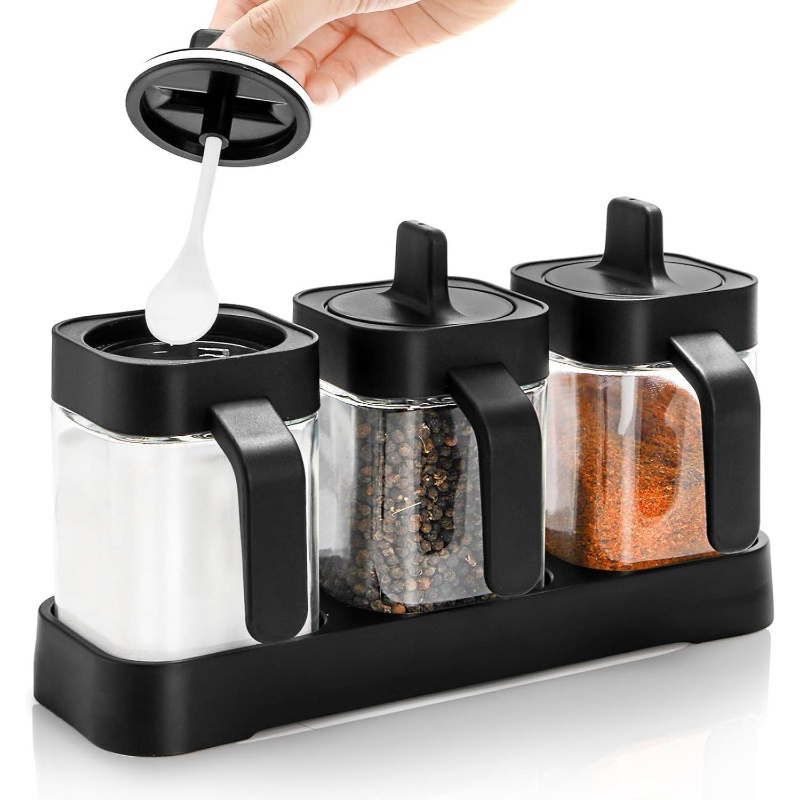 A set of three glass and wooden spice jars, with lids and spoons.